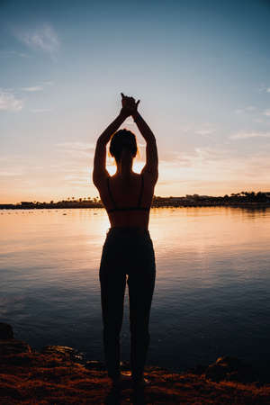 Young beautiful girl doing warm-up on the seashore. dawn.