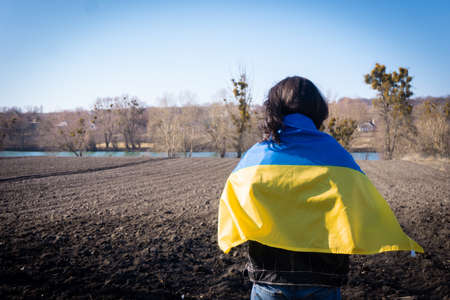 young man covered with the flag of ukraine in the field. patriotの写真素材