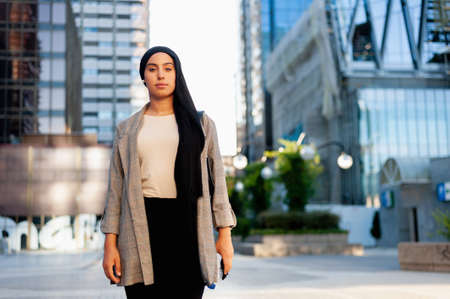 Portrait of a serious Muslim woman standing in an urban area looking at camera in a sunny day.の写真素材