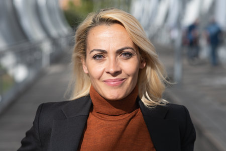 Close up portrait of a smiling blonde woman with formal clothes facing the camera in an urban streetの写真素材