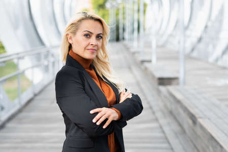 Adult blonde business woman standing with her arms crossed looking at camera in a urban landscapeの写真素材