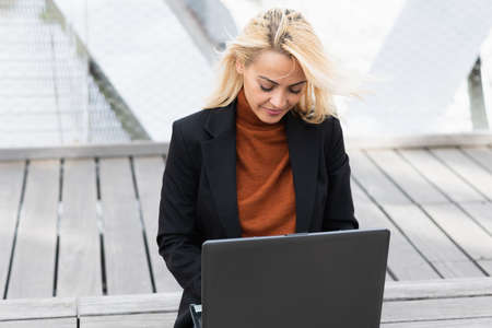 Portrait of a concentrated blonde adult businesswoman using a laptop outdoors in a cityの写真素材