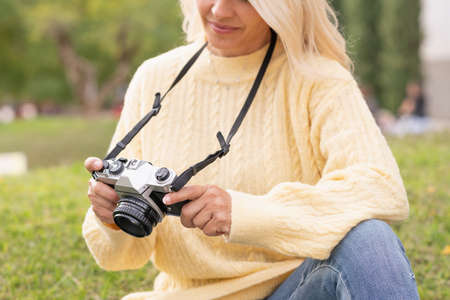Close up view of a woman holding a mirrorless digital camera while sitting on a parkの写真素材