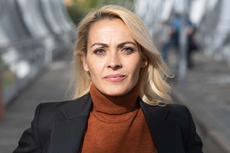 Close up portrait of a blonde adult woman with formal clothes facing the camera in an urban streetの写真素材