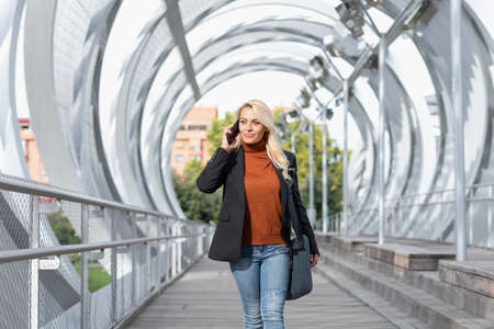 Photo with selective focus on a woman talking with the mobile while walking across an arched bridgeの写真素材