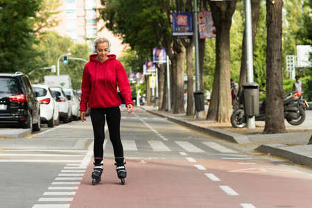 Blonde adult woman skating with inline skates along a city cycle pathの写真素材