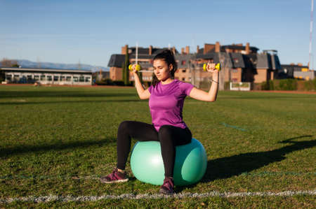 Woman sitting on fitball and doing exercises with dumbbellsの写真素材