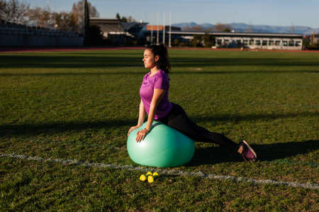 young woman doing exercise with a fitball on the grassの写真素材