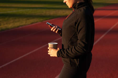 young athlete looks at the mobile while having a coffee on the running track