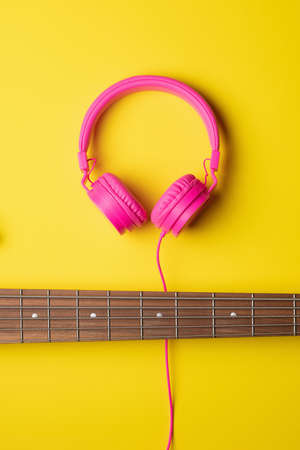 neck of a 5-string guitar placed horizontally and pink headsets on top of the neck, vertical plain backgroundの写真素材