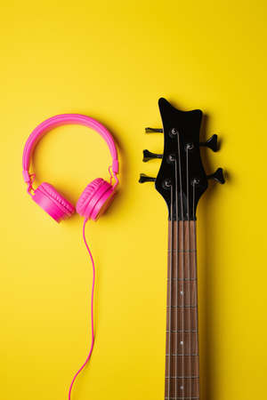 headband headphones fitted next to the head of a guitar over a plain yellow vertical backgroundの写真素材