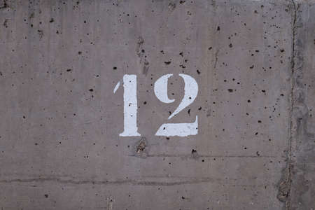 number 12 printed on a concrete wall full of small holes. Gray background