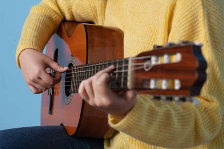 Studio photo with blue background of the hands of a woman playing a spanish classic guitarの写真素材
