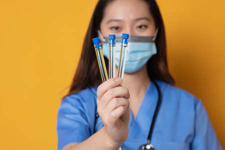 Studio photo with orange background of an asian doctor with mask showing laboratory samplesの写真素材