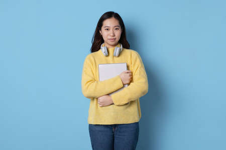 Studio photo with blue background of an asian student holding a folder while wearing headphones