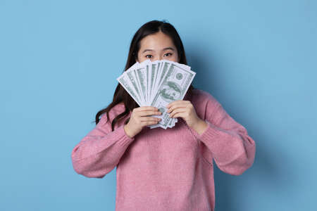 Studio photo with blue background of an asian woman showing a wad of banknotesの写真素材
