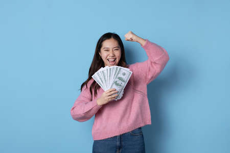 Studio photo with blue background of an asian woman showing a wad of banknotes while gesturing happyの写真素材