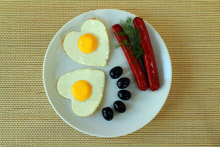 Fried eggs with sausage and olives on a dishの写真素材