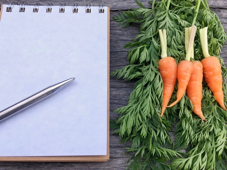Orange baby carrot put beside notebook and pen.の素材