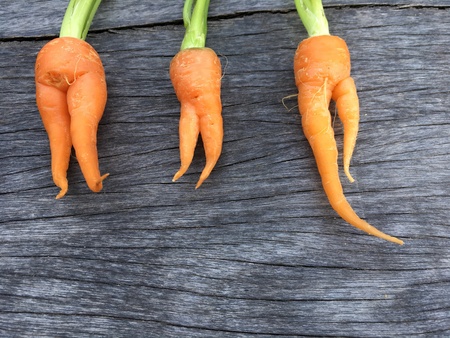 Orange baby carrot look like woman shape put on wooden background.の素材