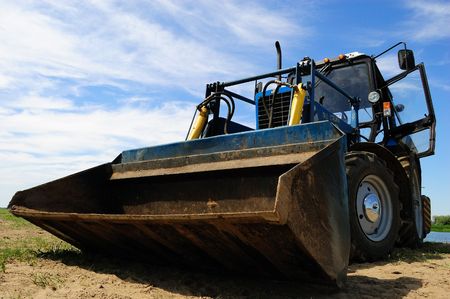 bulldozer at sandy riverside against blue sky, wide angle