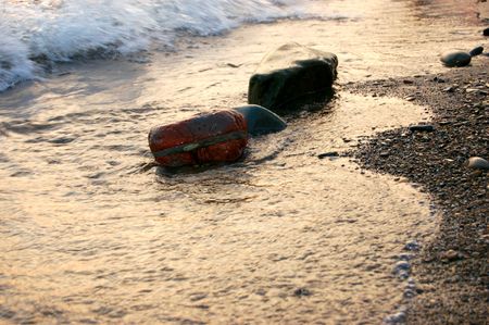 stones at sea shore covered with film of flowing water at sunsetの写真素材