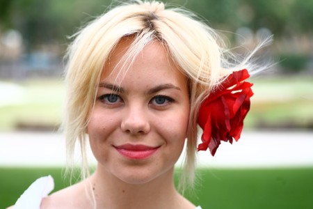 A stunningly beautiful young blond woman with red flower in hairの写真素材