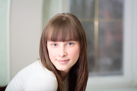 Portrait of a relaxed young woman smiling with hand on chin on sofa in living roomの写真素材