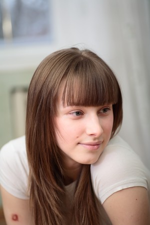 Portrait of a relaxed young woman smiling with hand on chin on sofa in living roomの写真素材