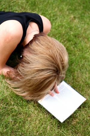 girl reading book outdoors laying on the green grassの写真素材