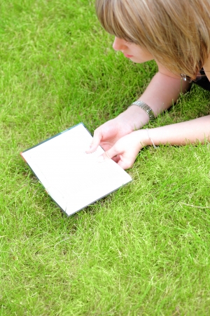 Beautiful young smiling woman laying on grass reading book, against green of summer park.の写真素材