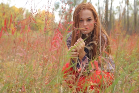 Portrait of a beautiful red-haired woman in red gloves sitting on the grassの写真素材