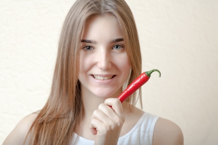 pretty blond woman head and shoulders shot holding in hands red spicy pepper on bege background. Healthy nutrition diet conceptの写真素材