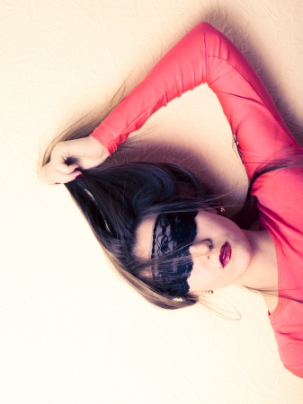 Sexy girl in black mask head and shoulders shot in pink party dress on beige background. Party costume conceptの写真素材