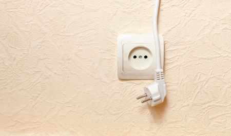 power outlet with plugged in cord closeup on beige. limited dof focus on outlet.