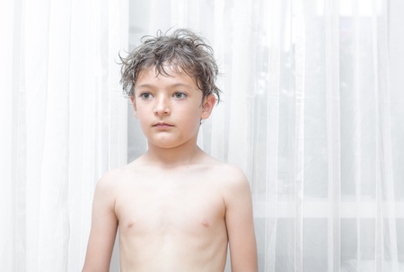 a happy smiling boy playing and having fun at home against white curtainの写真素材