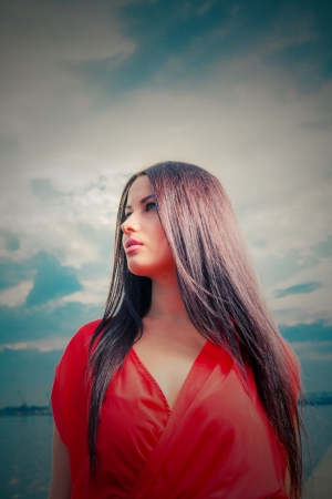 Brunette girl in red dress against dramatic sky  Outdoor fashion shotの写真素材