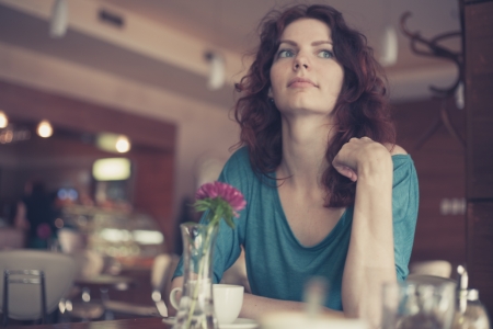 Waiting in loneliness - Young woman sitting in cafe on chair and looking away of cameraの写真素材