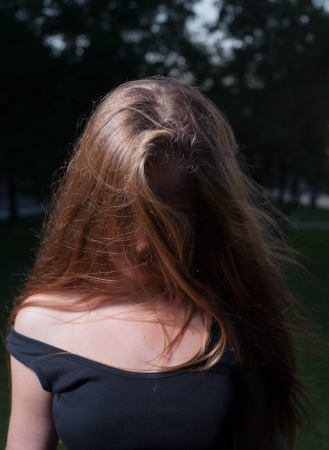 Face is hidden by hair. Sad 20s female outside close-up image. Portrait of a beautiful young 20s women in the park in evening.の写真素材