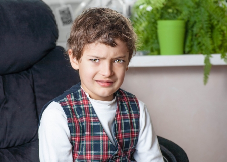 7 years old boy sitting in the chair  Sad boy looking at camera indoor shotの写真素材