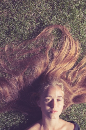 long haired blond girl lying on the grass and looking at camera. Toned imageの写真素材