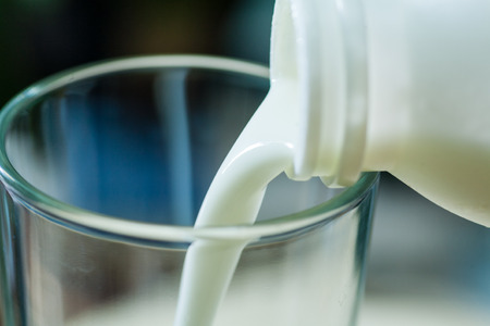 Fresh milk poured in glass cup over indoors backgroundの写真素材