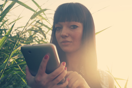 Backlit image of brunette using taplet pc outdoors in summerの写真素材