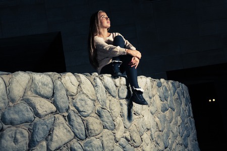Sporty blonde sitting on a big stone wall and looking up