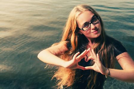 Young blonde makinf heart shape by her hands against waterの写真素材