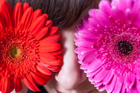 Young woman covering her eyes with fresh colorful flowers. Macro or very closeup shotの写真素材