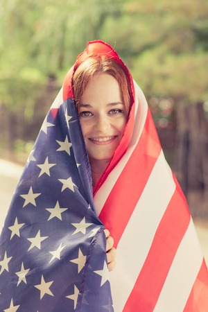 Smiling girl covered with US flag outdoors vertical shotの写真素材