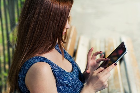 Redhead woman with tablet outdoors in profile viewの写真素材