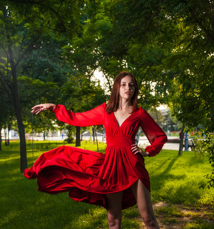 Young brunette dancing in red dress outdoors on nature . Portrait of dancing woman at forestの写真素材