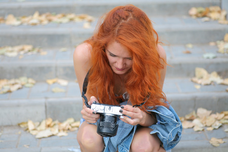 Young redhead woman photographer. Cute women halding modern camera in her hands and looking at screen inspect imagesの写真素材